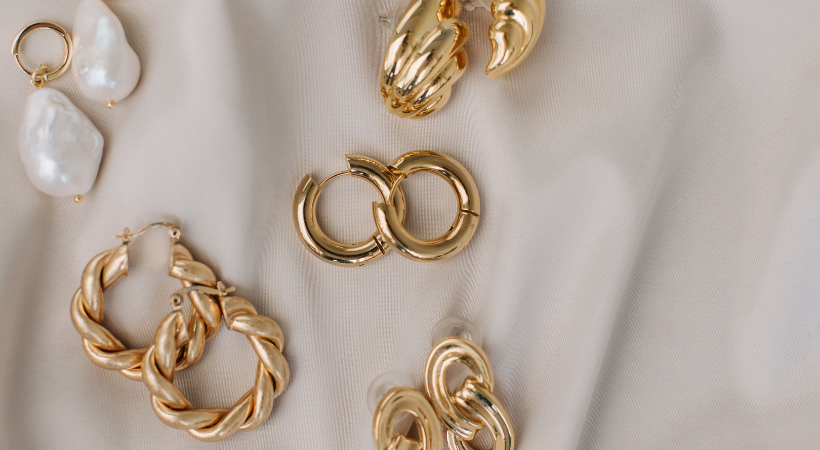 saten krem rengi bir örtü üzerinde gold renkli çelik küpeler var